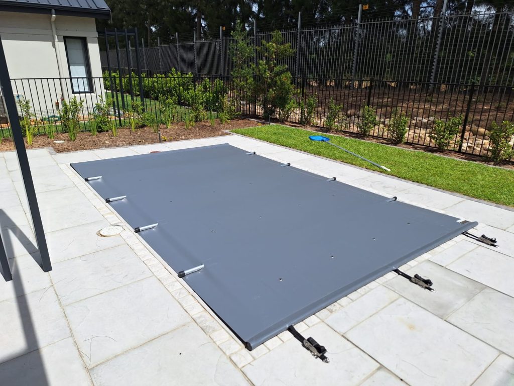 designer pool covers A backyard with a grey pool cover and a pool cover reel.
